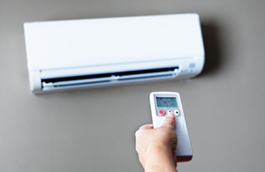 ai_ac_ductless Hand holding remote pointing at ductless AC unit