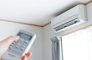 Hand holding remote pointed at ductless AC unit