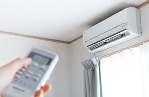 ai_ductless Hand holding remote pointed at ductless AC unit