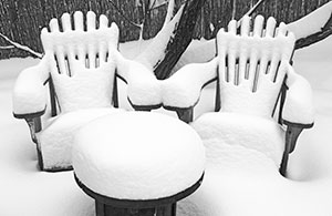 Snow covered yard with seats buried in snow.